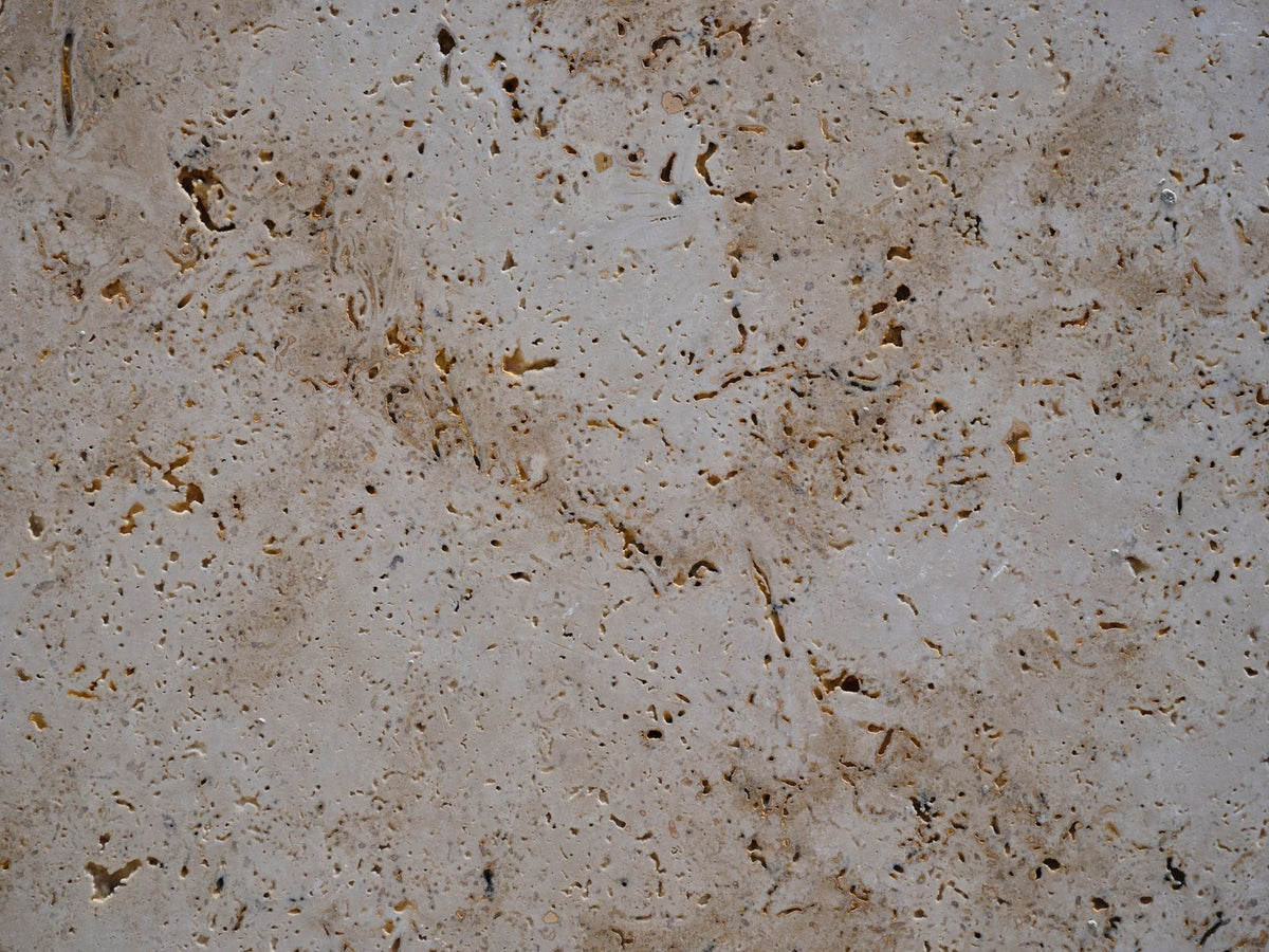 Dalle de travertin beige en lumière rasante, matière minérale pour illustrer l'autonomie et le temps de charge d'un diffuseur de parfum