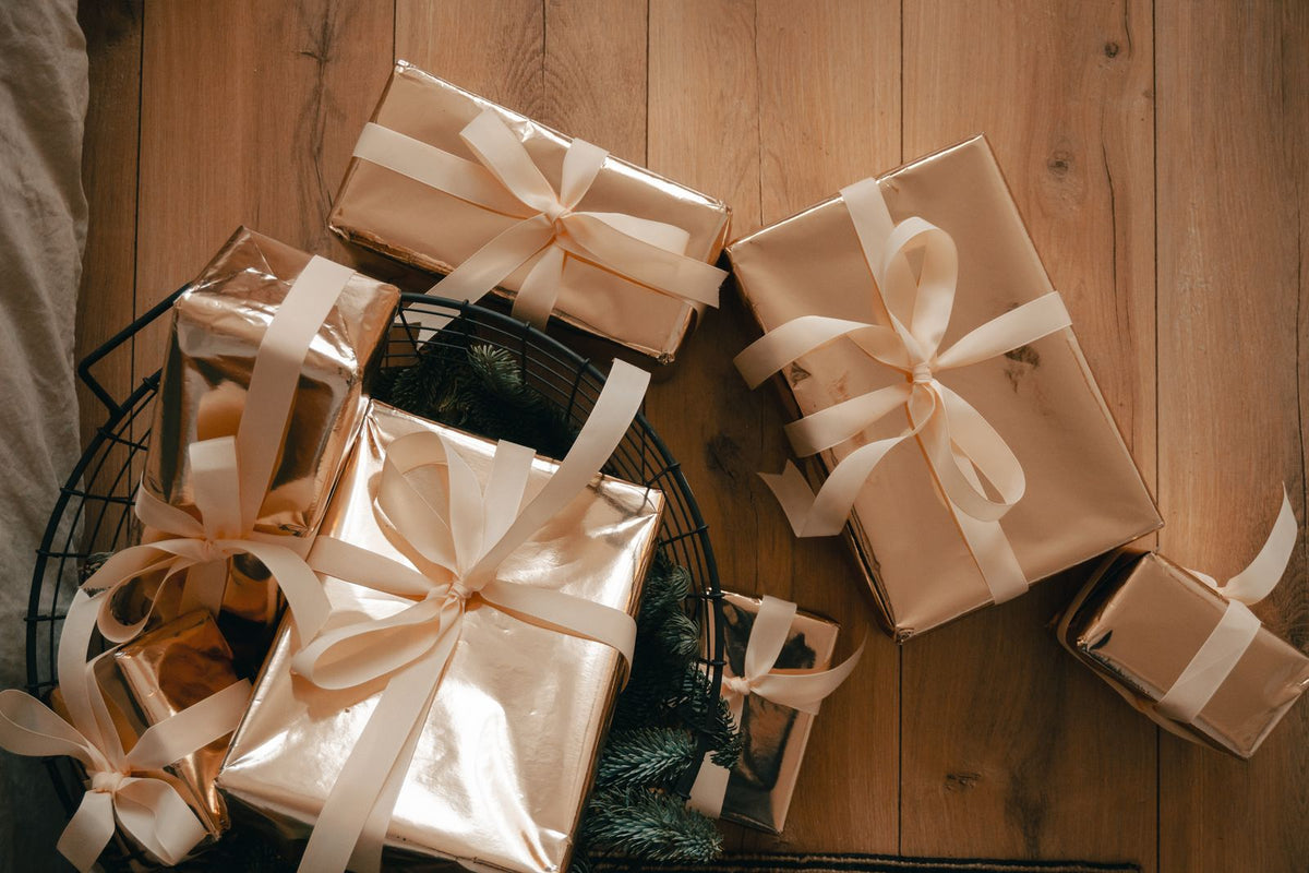 Plusieurs paquets cadeaux dorés à rubans crème réunis dans une corbeille sur un parquet clair, image d'un cadeau commun à plusieurs personnes