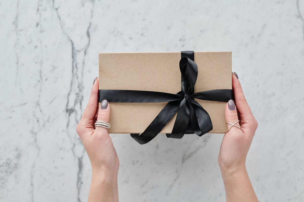 Deux mains tendent un paquet cadeau en papier kraft, une idee de cadeau pour quelqu un qui n aime pas les parfums