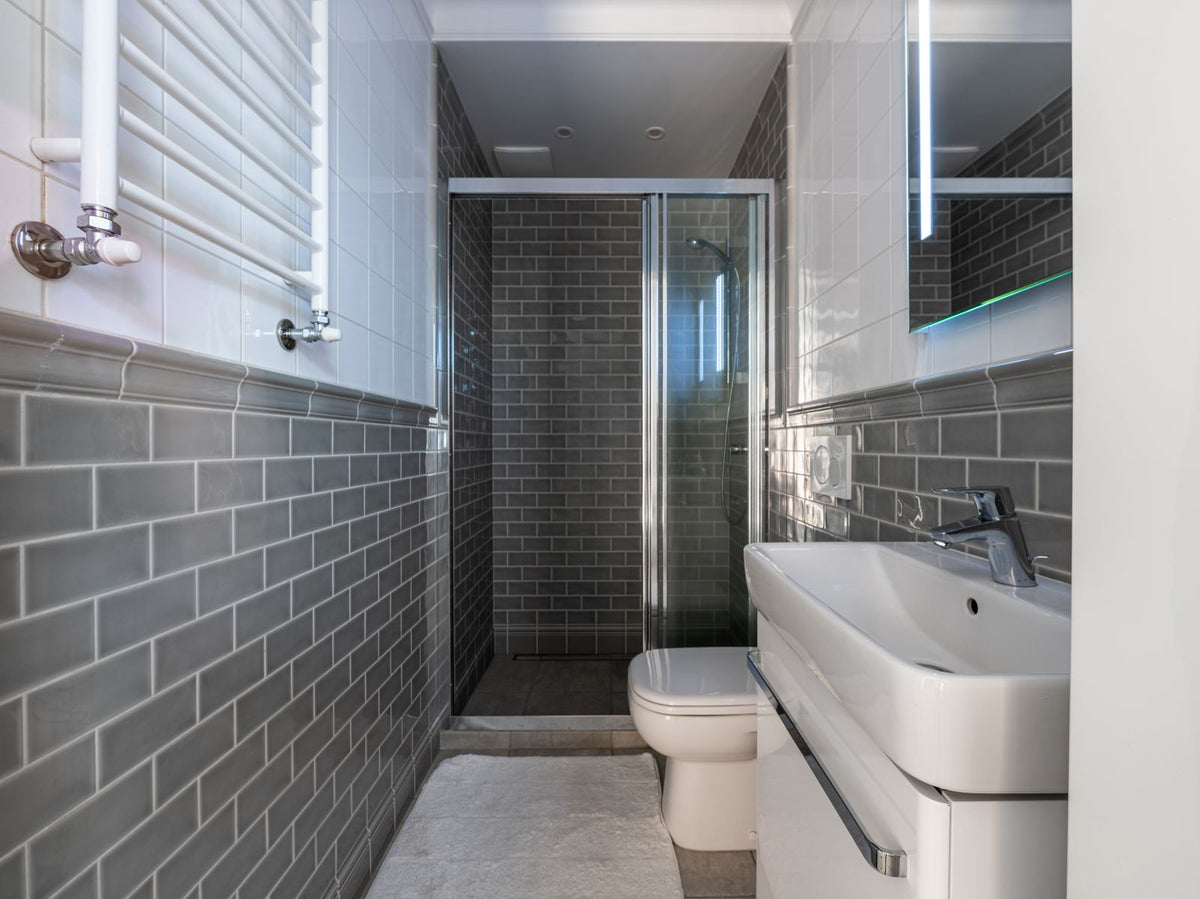 Salle de bain sans fenêtre qui sent le moisi : pièce étroite en carrelage métro gris, douche vitrée et vasque blanche