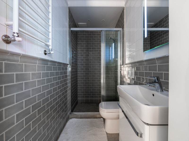 Salle de bain sans fenêtre qui sent le moisi : pièce étroite en carrelage métro gris, douche vitrée et vasque blanche